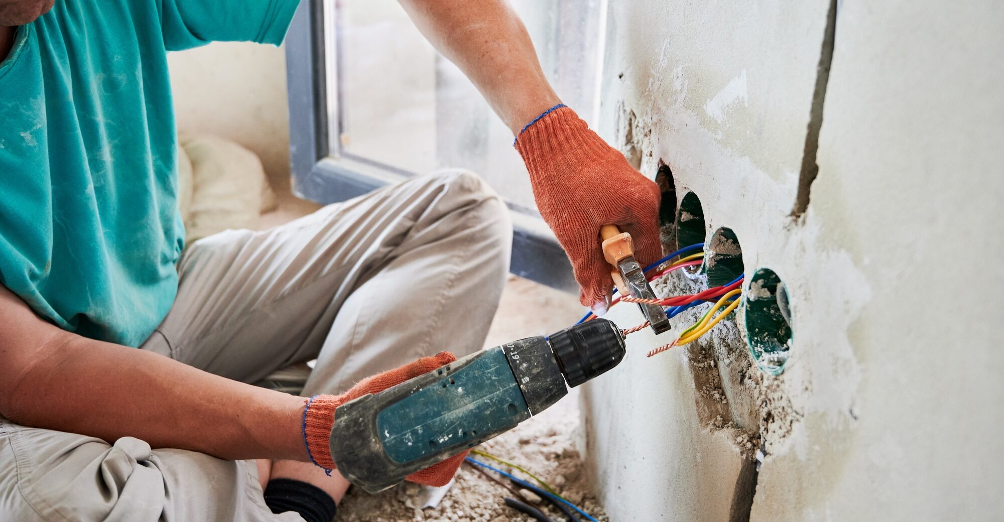 Male electrician using electric heat gun and pliers at home.